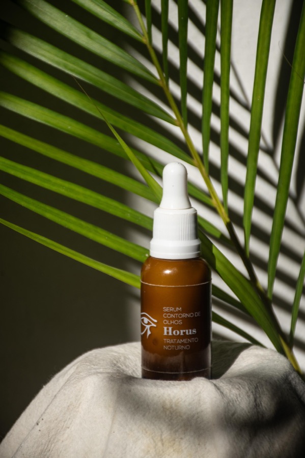 Sérum contorno de ojos con gotero, junto a una hoja de palmera
